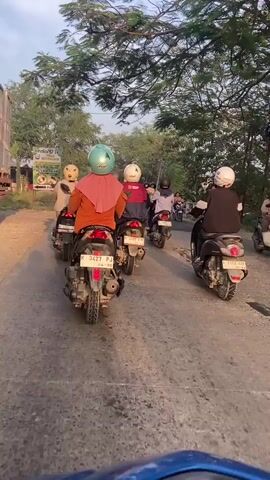 The video shows a group of people riding motorcycles on a dirt road. The motorcycles are moving in the same direction, and the people are wearing helmets. The road is lined with trees, and there is a truck in the distance. The sun is setting, and the sky is orange.