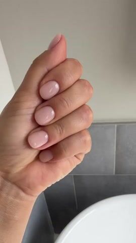 The media shows a close-up view of a person's hand, specifically their fingers and thumb. The hand has a light to medium skin tone and features neat, light pink manicured nails. The background consists of a light gray wall or ceiling and a tiled surface, possibly in a bathroom or similar area. The lighting suggests it is daytime, with soft, diffused light. The hand is moving, with the fingers opening and closing, and the thumb making gestures. In one instance, the hand is held up with all fingers spread, and in another, it's in a thumbs-up position. The overall impression is of a clean and well-maintained hand, possibly demonstrating a gesture or showing off the manicure. There is no visible text in the media. The context of Houston, USA, does not provide any specific visual cues within the media itself.