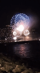 Fireworks light up the waterfront against a glowing city skyline