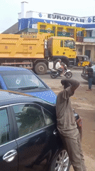Man in uniform leans against car on Nigerian street