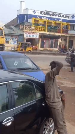 Man in uniform leans against car on Nigerian street