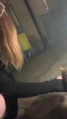 The video begins with a close-up shot of a tabby cat being petted by a hand. The cat is wearing a pink and yellow collar. The background is blurred, but appears to be an outdoor setting at night, with some lights visible. The camera then shifts to a slightly wider view, showing more of the cat and the person petting it. The person's arm is visible, wearing a black sleeve. The cat's face is visible, and it appears to be looking towards the camera. The video continues with close-ups of the cat's face and body, and then the scene briefly changes to show the person holding the cat closer to the camera. The background continues to be blurred, but some trees and lights are visible. The video ends with a close-up of the cat's face.