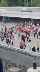 Sports fans in red and white gather near bridge plaza