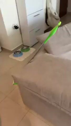 The video pans through an apartment showing a sofa, pillows, a table, a manicure station set up with lamps, a nail drill, and bottles, and a person holding up two fingers in a peace sign.  The room has white walls and curtains.
