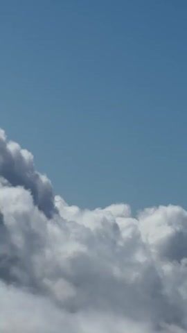 The video shows a close-up view of clouds and the sky. The clouds are white and fluffy, with some darker gray areas indicating depth and shadow. The sky is a clear blue. The camera appears to be moving slightly, giving a sense of looking through the clouds. There are no people or objects visible in the video. The overall impression is one of a peaceful and serene sky.