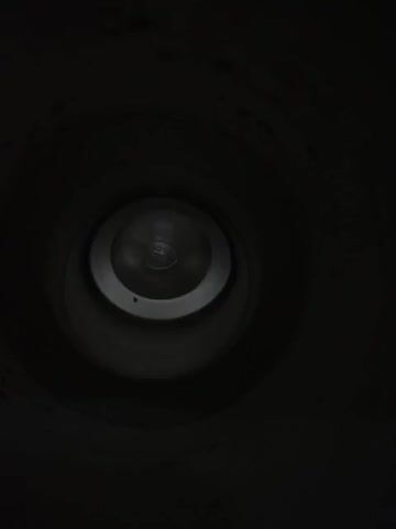 The video shows a close-up view looking down into the opening of a metal container, likely a thermos or a mug. The lighting is dim, and the interior of the container is visible. The camera slowly moves downwards, providing a slightly different perspective of the inner workings of the container's bottom. The bottom appears to have a layered or recessed structure, with a circular indentation at the very center. Some minor smudges or debris are visible on the inner walls of the container. The overall impression is of an empty, industrial-style metal vessel.