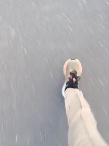 This is a first-person perspective video of someone rollerblading. The camera is pointed down at the rollerblader's feet and the pavement. The rollerblader is wearing tan pants and tan rollerblades with pink accents. The pavement appears to be asphalt. The video is slightly shaky, indicating movement.