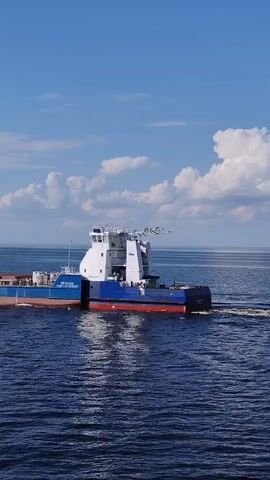 The video shows a tugboat navigating on a body of water on a sunny day with clouds in the sky. The tugboat has a blue and white color scheme with the name "NY02000" visible on its side. The water is deep blue and the tugboat leaves a trail as it moves through the water. The scene is well-lit, creating clear visuals of the tugboat and its surroundings.