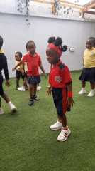 Children in school uniforms dance outdoors with teacher