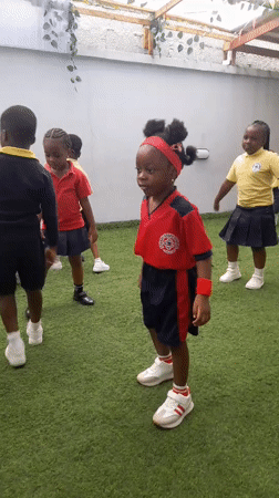 Children in school uniforms dance outdoors with teacher