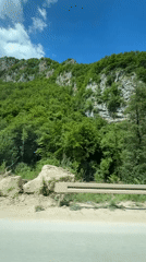 Vehicle travels road in Klanac, Bosnia alongside forested hillside