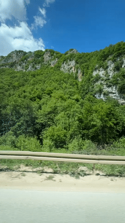 Vehicle travels road in Klanac, Bosnia alongside forested hillside
