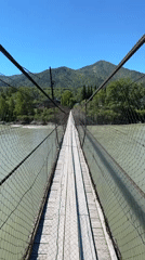 Pedestrian crosses suspension bridge over green river in Russia