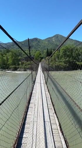 Pedestrian crosses suspension bridge over green river in Russia