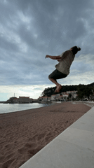 Man performs backflip on Petrovac beach during cloudy afternoon