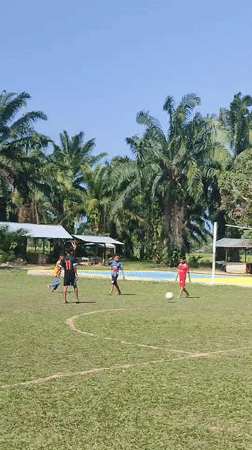 Five people play casual soccer in sunny Blangriek, Indonesia
