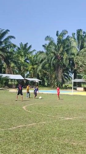 Five people play casual soccer in sunny Blangriek, Indonesia