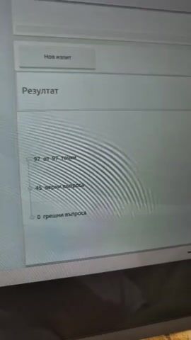 A close-up shot captures an HP laptop screen displaying a digital test or exam interface. The video begins by showing a green checkmark animation, signaling a successful completion or correct answer. The screen then transitions to a results page.

The visible text on the screen is in Bulgarian (Cyrillic script). The results show a perfect score: "97 от 97 точки" (97 out of 97 points), "45 верни въпроса" (45 correct questions), and "0 грешни въпроса" (0 wrong questions). Other visible text includes "Нов изпит" (New exam) and "Резултат" (Result). Partially visible text includes "Изпитна листовка № 24399079" (Exam sheet No. 24399079).

The laptop is black with the silver "hp" logo visible at the bottom of the screen frame. The surface beneath the laptop appears to be a soft, patterned fabric in yellow and white, possibly a blanket or bedspread. The lighting suggests an indoor setting. The video captures the moment of revealing an excellent test performance.