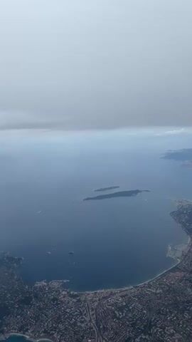 The video shows an aerial view of a coastline with a city, a bay, and islands in the distance. The sky is overcast, and as the video progresses, the view is obscured by increasing cloud cover, eventually leading to a completely white and gray screen.