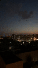 Crescent moon rises over illuminated city skyline at dusk