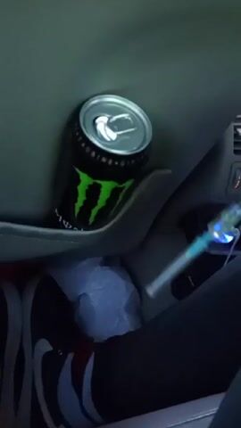 Here is a description of the video.
The video shows a can of Monster energy drink and a syringe. The syringe appears to be filled with a yellowish liquid. The background is blurry, but it seems to be inside a car.