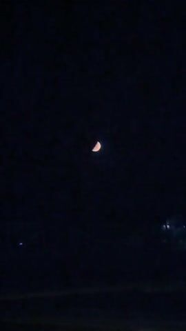 A video shows a half-moon in a dark sky. The moon is illuminated on the right side and is orange-yellow in color. The background is a deep, uniform dark blue, suggesting it is nighttime. There are no other visible celestial bodies or objects in the frame. The video appears to be a static shot with no movement, focusing solely on the moon.
