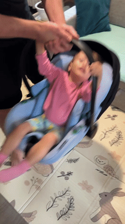 Adult plays with laughing child in car seat indoors