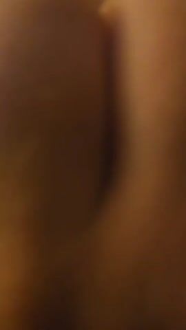 The video shows a close-up, blurry shot of skin. The lighting is dim, casting shadows and highlighting the texture of the skin. The focus is on a curved surface, possibly a body part, with a dark line or crease running through the center. The colors are predominantly warm browns and tans.