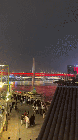 Crowds gather at Chongqing waterfront viewing illuminated bridge cityscape