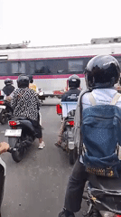 Motorcyclists queue at a railway crossing as a train passes