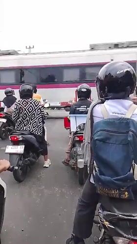 Motorcyclists queue at a railway crossing as a train passes