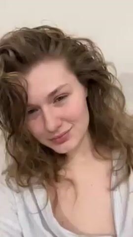 The video shows a woman in light blue striped pajamas. She has wavy light brown hair and appears to be indoors. She is touching her hair and smiling at the camera, while music plays in the background.