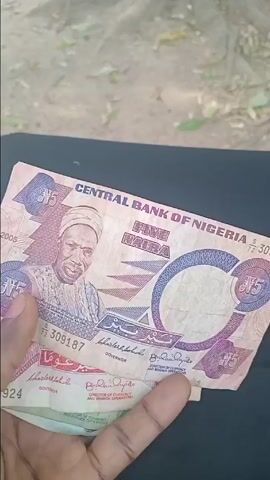 The video showcases a collection of old Nigerian currency banknotes, held in a person's hand. The background appears to be an outdoor setting with dry ground and some foliage. The hand is holding the notes over a black surface, possibly a lap or a table.

The notes are displayed one by one:
1.  **5 Naira note (0:00 - 0:08):** This note is pink/purple in color and features the portrait of Sir Abubakar Tafawa Balewa. The text "CENTRAL BANK OF NIGERIA FIVE NAIRA" is clearly visible. The year "2005" is also printed on the note.
2.  **10 Naira note (0:10 - 0:15):** This note is predominantly red/pink and displays the portrait of Obafemi Awolowo. The text "CENTRAL BANK OF NIGERIA TEN NAIRA" is visible. It also bears the year "2005".
3.  **20 Naira note (0:17 - 0:22):** This note has a greenish-brown hue and features the portrait of General Murtala Muhammed. The text "CENTRAL BANK OF NIGERIA TWENTY NAIRA" is present. This note also shows the year "2005" and appears slightly more worn than the others.
4.  **50 Naira note (0:24 - 0:30):** This note is light blue/white and features multiple portraits representing various indigenous tribes of Nigeria. The text "N50 NAIRA CENTRAL BANK OF NIGERIA" is visible. This note also displays the year "2005".

The person holding the notes narrates, identifying each denomination and the historical figure or group depicted on it. The camera focuses on each note as it's being presented.