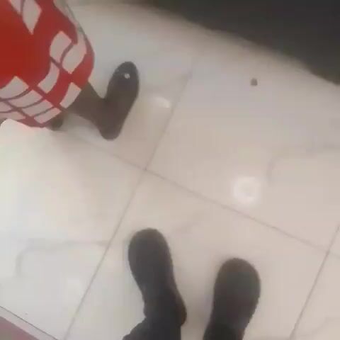 The camera moves from eye level to point toward the floor, and then back up toward the upper shelves in a corner grocery store.  The aisle contains shelf space, a check out stand, and a poorly lit Christmas tree.  The camera continues moving toward the floor and rests on a small packet of an undefined, red-colored product. The room appears to be busy with customers.