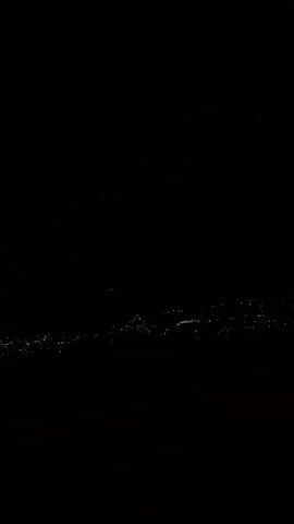 The video shows a long-distance shot of city lights at night. The lights are scattered across a dark landscape, with the sky being completely black. There's no specific subject, person, or action visible other than the distant city lights.