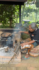 Elderly woman roasts coffee beans over traditional oven in Tampaksiring