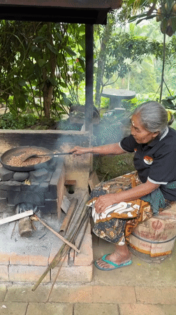 Elderly woman roasts coffee beans over traditional oven in Tampaksiring