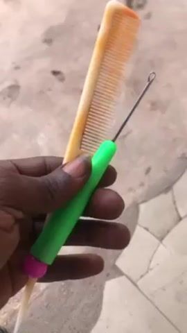 A dark-skinned hand holds a light yellow comb and a metal latch hook tool with a green handle and pink end. The background is a tan and gray tiled surface. The hand rotates to show the tools from different angles.