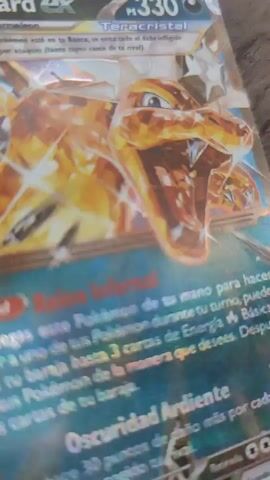 The video displays a collection of Pokémon trading cards laid out on a wooden surface. The camera pans slowly across the cards, showcasing their designs and text.

The primary subject is a "Charizard ex" Teracristal card with 330 HP, featuring a prominent, shiny, crystalline Charizard illustration. Other cards visible include a "Gengar" V or VMAX, a "Vaporeon V" Black Star Promo (SWSH150), a "Jolteon VMAX" (051/203 from Evolving Skies), and a "Blastoise ex." All cards are in Spanish.

Notable visible text includes:
*   **Charizard ex:** "Habilidad Reino Infernal" (Ability Infernal Realm) and "Oscuridad Ardiente" (Burning Darkness) attack details. Card number 125/197.
*   **Gengar:** "Habilidad" (Ability) with partial text regarding moving damage counters. Card number 047/073.
*   **Vaporeon V:** "Roba 3 cartas" (Draw 3 cards) and "Salto Salpicadura" (Splash Jump) attack.
*   **Jolteon VMAX:** "Maxirretroceso" (Max Reversal) attack with text indicating damage to benched Pokémon.
*   **Blastoise ex:** "Habilidad Caparazón de Combate" (Ability Battle Shell) and "Cañon de Agua" (Hydro Cannon) attack. Card number 009/165.

The cards are well-lit, suggesting daytime viewing. The setting appears to be indoors, likely on a table or desk in Sant Just Desvern, Spain, given the language of the cards. There are no people visible, and no specific activity beyond displaying or examining the cards is shown.