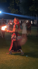 Fire dancer performs traditional torch routine on grass at night