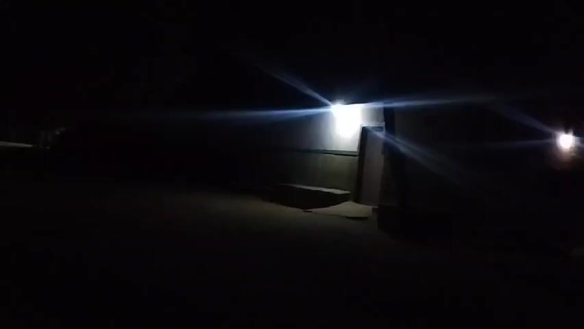 At night, a person speaks in a dark environment. Briefly, bright lights appear in the distance and then move closer.