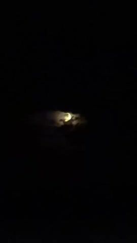 The video shows a night sky with the moon partially obscured by clouds. The moon appears as a bright, yellowish orb, peeking through wispy, dark clouds. The overall scene is dark, with the blackness of the night sky dominating the frame, allowing the illuminated moon and clouds to stand out. The camera seems to be pointing upwards, capturing a view of the celestial bodies. There are no people or man-made objects visible in the frame. The time of day is clearly night, and the presence of clouds suggests some atmospheric conditions, though no specific weather events like rain or wind are evident from the static image. The location context provided is Chirsova, Moldova, which helps to establish a geographical setting, but there are no visual cues within the image itself that would specifically identify this location. The mood of the image is one of quiet contemplation, with the celestial display offering a natural spectacle. There is no visible text in the media file.