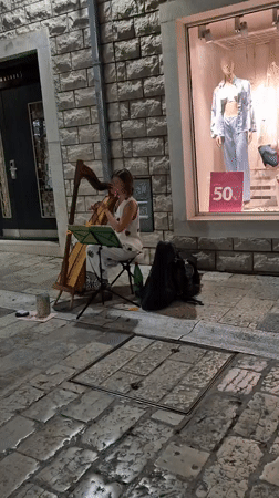 Harp music on cobblestones beside a sale window in Herceg Novi
