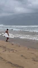 Surfer approaches ocean under overcast skies in Ahangama
