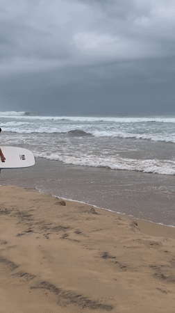 Surfer approaches ocean under overcast skies in Ahangama