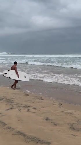 Surfer approaches ocean under overcast skies in Ahangama