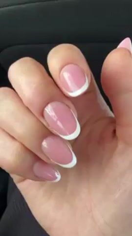 The video displays a hand with manicured fingernails. The nails are short to medium in length and oval-shaped. They have a light pink base color with a white tip in the style of a French manicure. The hand is set against the background of a vehicle interior, specifically a dark gray or black upholstered seat. The hand moves slightly during the video, showing both the palm and the back of the hand. The skin tone of the hand is light. The lighting appears to be natural daylight. The overall focus is on the appearance of the nails.