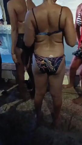 The video shows a group of women standing or dancing by a pool at night. They are dressed in swimwear or other revealing clothing. The camera focuses on the women from behind. There are no interactions apparent. The environment appears to be a casual party setting.