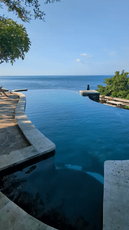 Woman swims in infinity pool overlooking ocean in Abang
