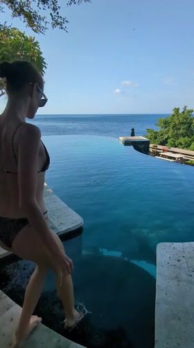 Woman swims in infinity pool overlooking ocean in Abang